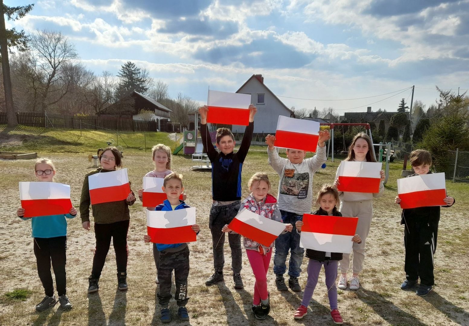 Wychowankowie Placówki Wsparcia Dziennego w Sulechowie przed świetlicą, pozują z własnoręcznie wykonanymi flagami. 