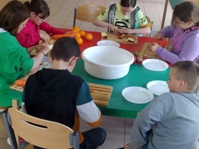 Zdjęcie przedstawia wychowanków obierających i krojących owoce i warzywa na sok.