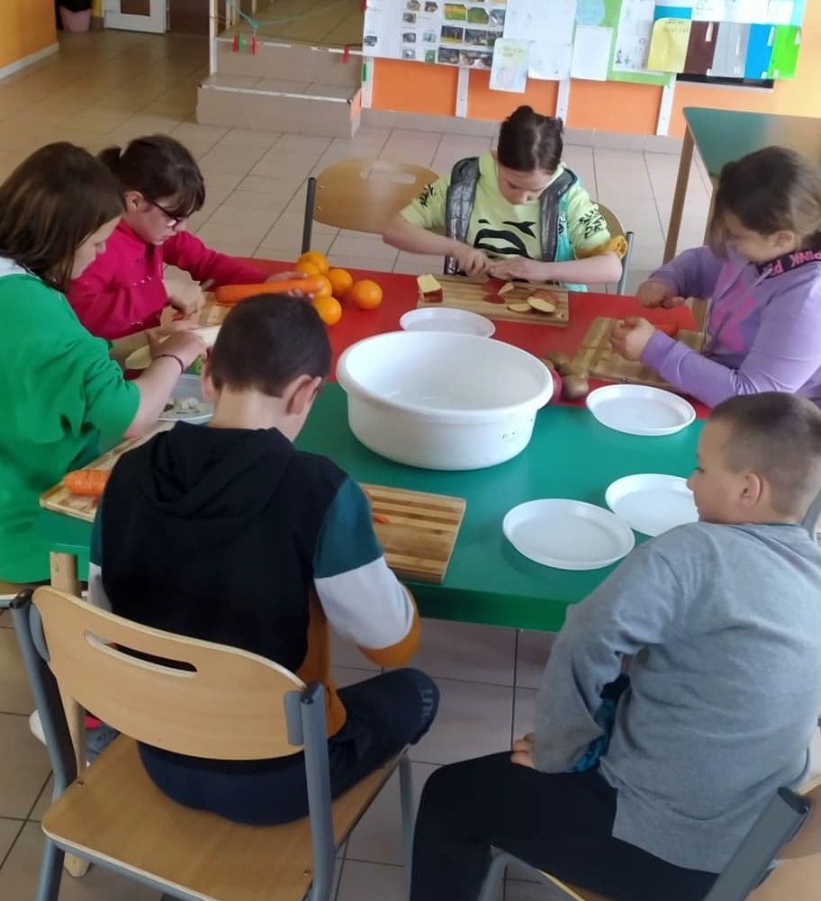 Zdjęcie przedstawia wychowanków obierających i krojących owoce i warzywa na sok.