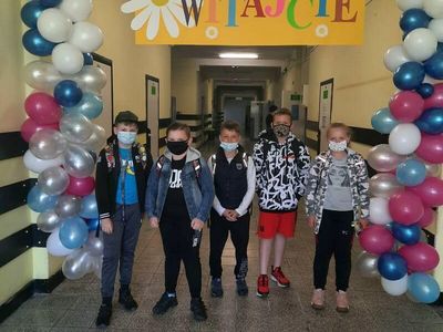 Uczniowie klasy ósmej przy powitalnej bramie z balonów, cieszą się z powrotu do szkoły w formie stacjonarnej.