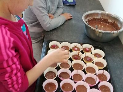 Dziewczynka z Placówki Wsparcia Dziennego w Kusicach dodająca do każdej muffinki malinę lub borówkę.