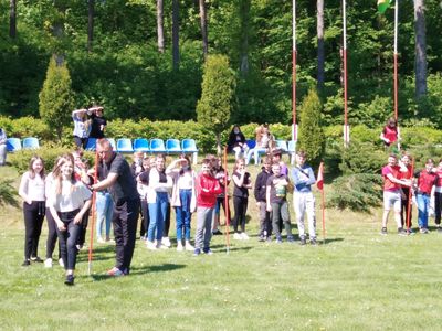 Uczniowie Szkoły Podstawowej w Lejkowie podczas zawodów i konkurencji sportowych na boisku szkolnym, na pierwszym planie również nauczyciel wychowania fizycznego.