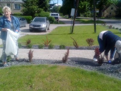 Zdjęcie seniorki, która pozuje z workiem na śmieci oraz dwóch innych kobiet podczas oczyszczania terenu rekreacyjnego przy Domu Wiejskim w Ostrowcu.