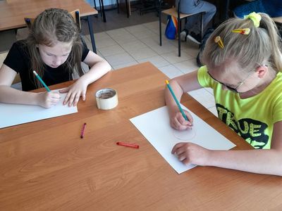  Dwie dziewczynki z Placówki Wsparcia Dziennego w Sulechowie wykonujące prace plastyczne, w tle dwóch chłopców i dziewczynka.