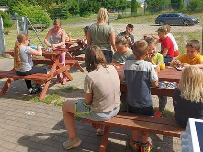 Wychowankowie Placówki Wsparcia Dziennego w Laskach, którzy jedzą naleśniki na świeżym powietrzu.