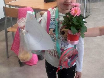 Dziewczynka pozuje z przygotowaną kompozycją kwiatową oraz laurką dla swojej mamy.
