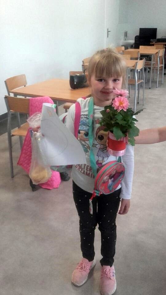 Dziewczynka pozuje z przygotowaną kompozycją kwiatową oraz laurką dla swojej mamy. 