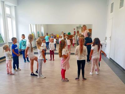 Grupa dzieci w kółku uczestniczy w zajęciach rytmiki w Świetlicy Kultury w Malechowie, dzieci wykonują polecenia instruktorki. 
