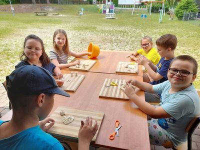 Wychowankowie Placówki Wsparcia Dziennego w Sulechowie podczas przygotowywania masy solnej, siedzą przy stoliku na dworze i pracują z masą solną.