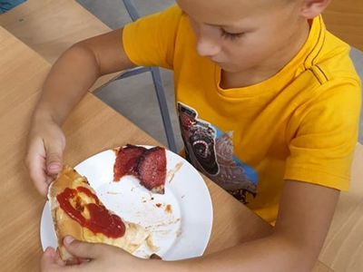 Chłopiec z kawałkiem pizzy wykonanej podczas warsztatów kulinarnych w Świetlicy Kultury w Malechowie. 