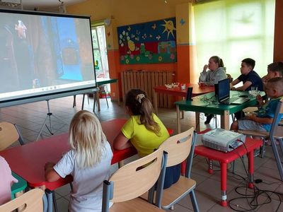 Wychowankowie z Placówki Wsparcia Dziennego w Laskach oglądają bajkę na dużym ekranie, na drugim planie ekran.