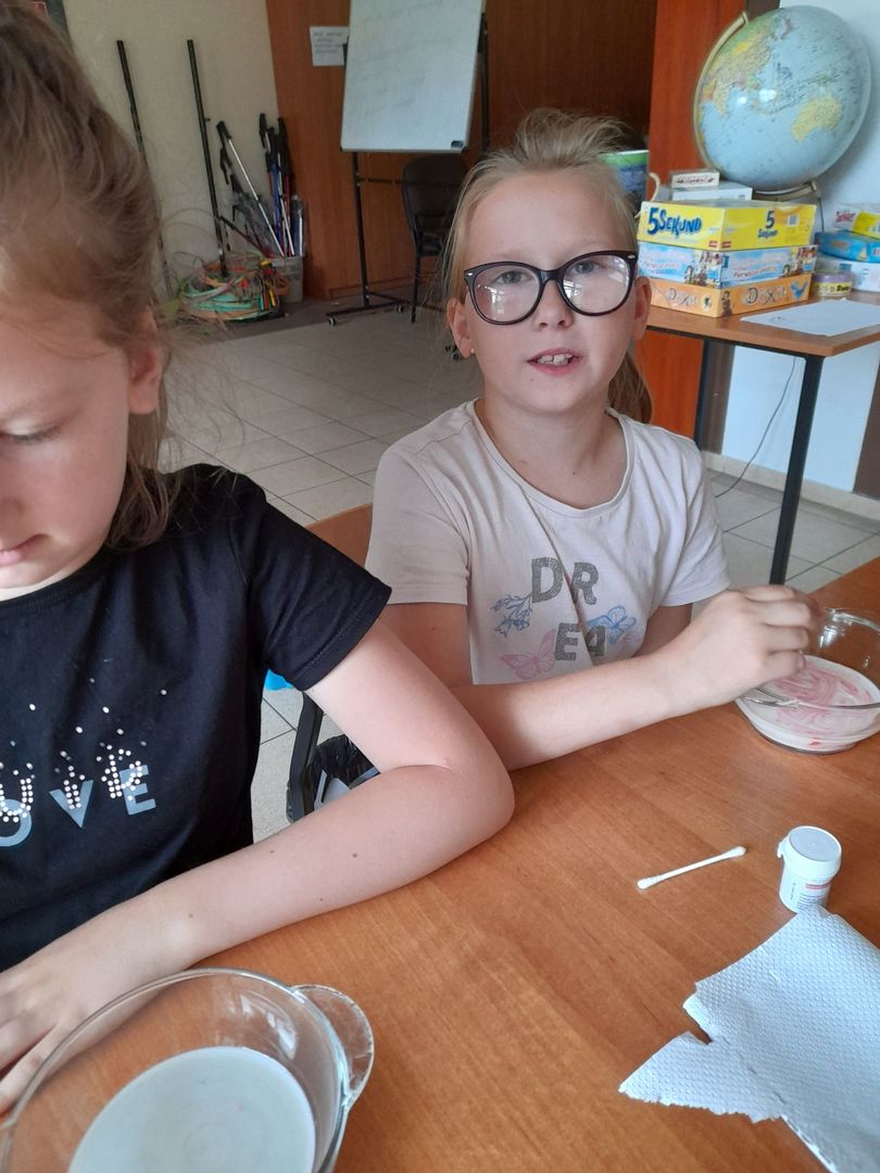 Dwie dziewczynki z Placówki Wsparcia Dziennego w Sulechowie wsypują barwniki spożywcze do mleka.