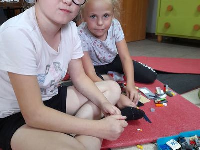 Dwie dziewczynki z Placówki Wsparcia Dziennego w Sulechowie , siedzące na matach gimnastycznych i budujące z klocków Lego.