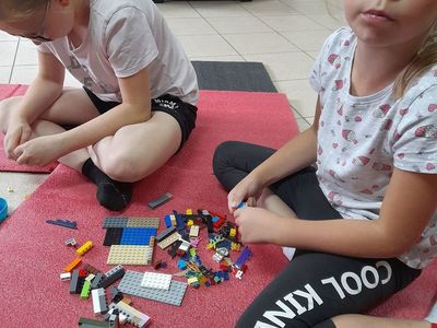 Dwie dziewczynki z Placówki Wsparcia Dziennego w Sulechowie , siedzące na matach gimnastycznych i pozujące z klockami Lego.