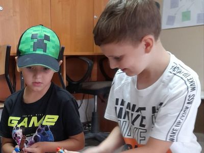 Dwóch chłopców z Placówki Wsparcia Dziennego w Sulechowie, siedzący na matach gimnastycznych i oglądający ludziki z klocków Lego.