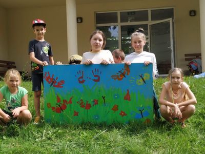 Dzieci z Placówki Wsparcia Dziennego w Gorzycy przed świetlicą wiejską z wykonaną przez nich pracą z odbitymi rączkami.