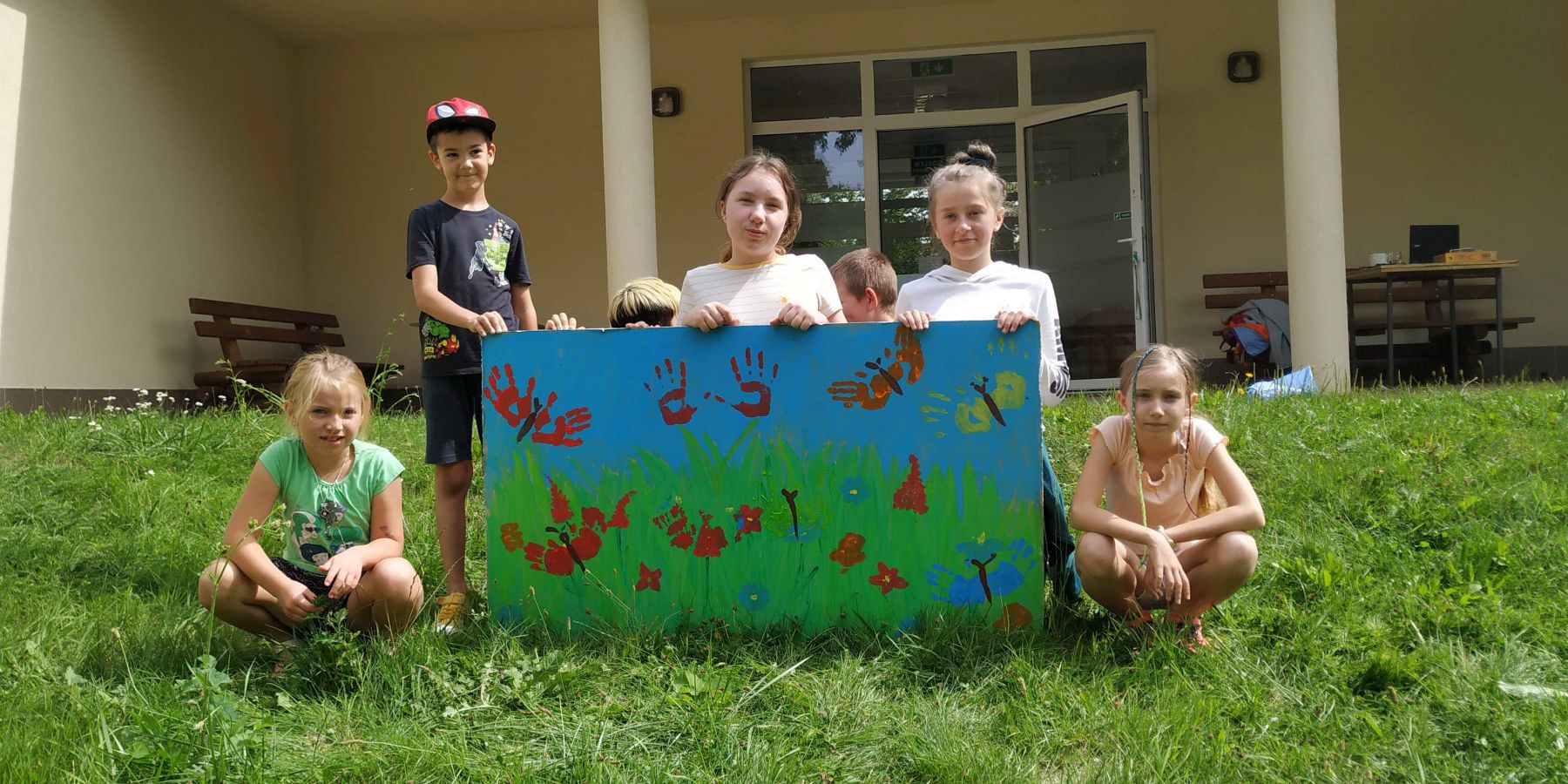 Dzieci z Placówki Wsparcia Dziennego w Gorzycy przed świetlicą wiejską z wykonaną przez nich pracą z odbitymi rączkami.