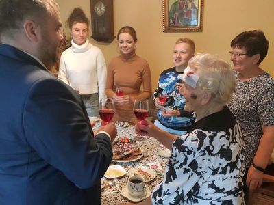 Wójt Radosław Nowakowski i 95-letnia Genowefa Góraj oraz jej rodzina śpiewają Dwieście Lat przy symbolicznej lampce szampana.  