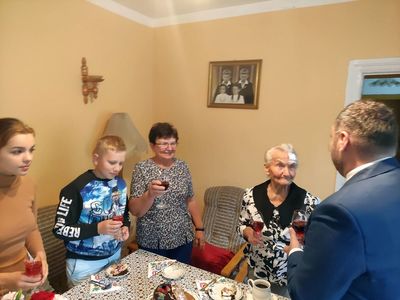 Wójt Radosław Nowakowski i 95-letnia Genowefa Góraj i jej rodzina śpiewają Dwieście Lat przy symbolicznej lampce szampana.  