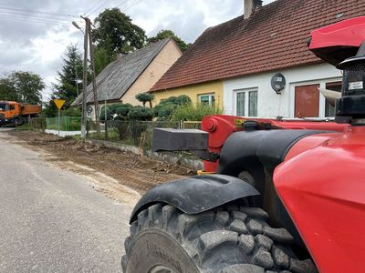 Remontowana droga i chodnik, rozjeżdżony teren i traktor. 