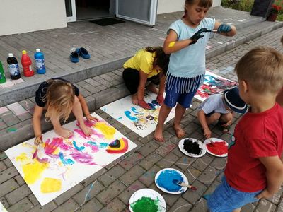 Dzieci przed świetlicą w Kusicach malują rączkami i stopami, odbijają je na papierze.