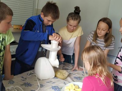 Dzieci z Placówki Wsparcia Dziennego w Gorzycy przygotowują pulpę z ziemniaków do placków. Chłopiec "przepuszcza" ziemniaki przez maszynkę, obserwują go inni wychowankowie.