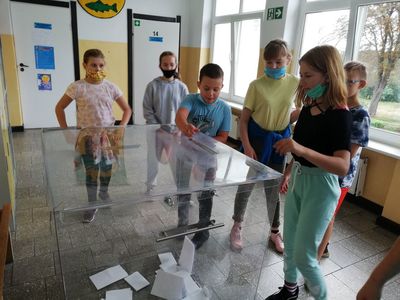 Chłopiec ze Szkoły Podstawowej w Lejkowie wrzuca swój głos do urny, obserwują to cztery dziewczynki i dwóch chłopców. 