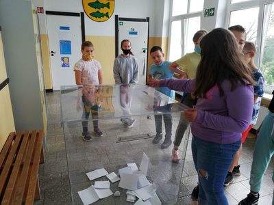 Dziewczynka ze Szkoły Podstawowej w Lejkowie wrzuca swój głos do urny, obserwują to jej koledzy. 