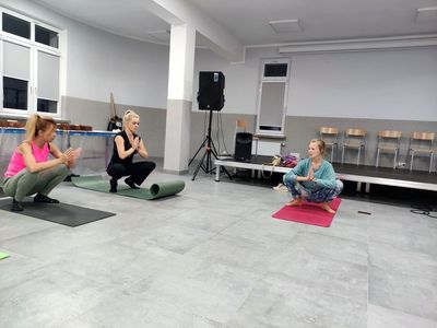 Instruktorka jogi na macie i dwie panie, które wykonują ćwiczenia.