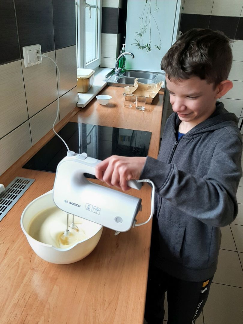 Wychowanek Placówki Wsparcia Dziennego w Przystawach przygotowuje ciasto, mieszkając żółtka z cukrem mikserem. 