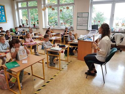 Mama Oliwii z klasy pierwszej Szkoły Podstawowej w Malechowie czyta fragment książki, dzieci słuchają uważnie. 