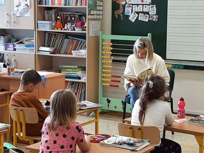 Mama Zosi z klasy pierwszej Szkoły Podstawowej w Malechowie czyta fragment książki, dzieci słuchają uważnie. 