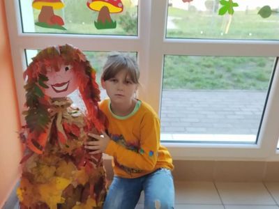 Dziewczynka z Placówki Wsparcia Dziennego w Laskach z Panią Jesień wykonaną z papieru i kolorowych liści.
