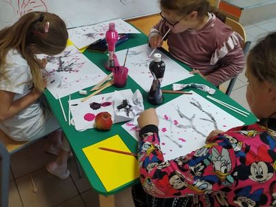 Dzieci z Placówki Wsparcia Dziennego w Laskach malują farbami kolorowe drzewka.