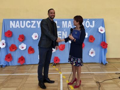 Dyrektor Zespołu Szkół wręcza nagrodę nauczycielowi, wspólnie pozują do zdjęcia.