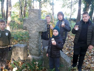 Wychowankowie Placówki Wsparcia Dziennego w Kosierzewie przy grobie na zabytkowym cmentarzu, zapalają znicze.