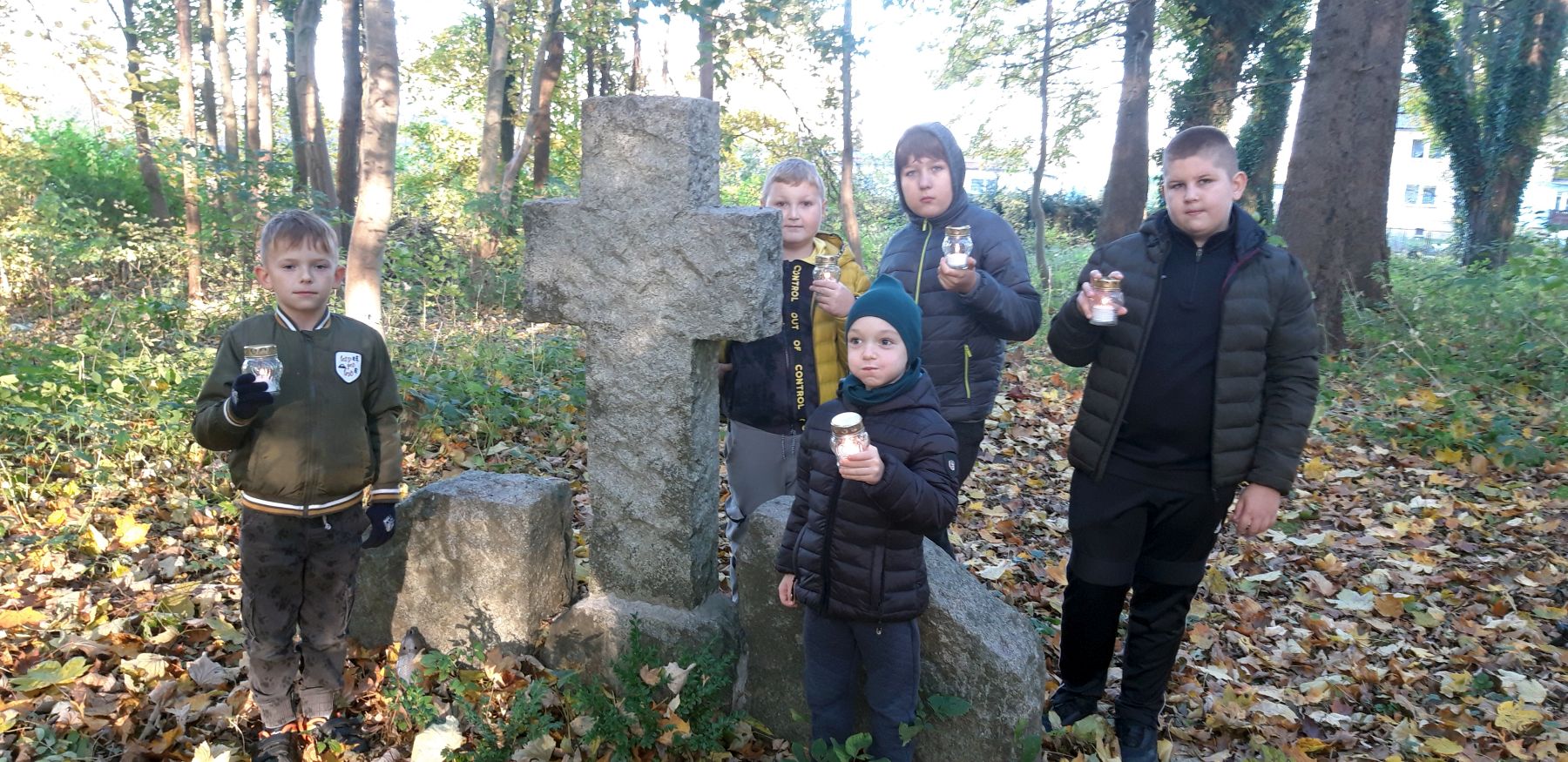 Wychowankowie Placówki Wsparcia Dziennego w Kosierzewie przy grobie na zabytkowym cmentarzu, zapalają znicze.