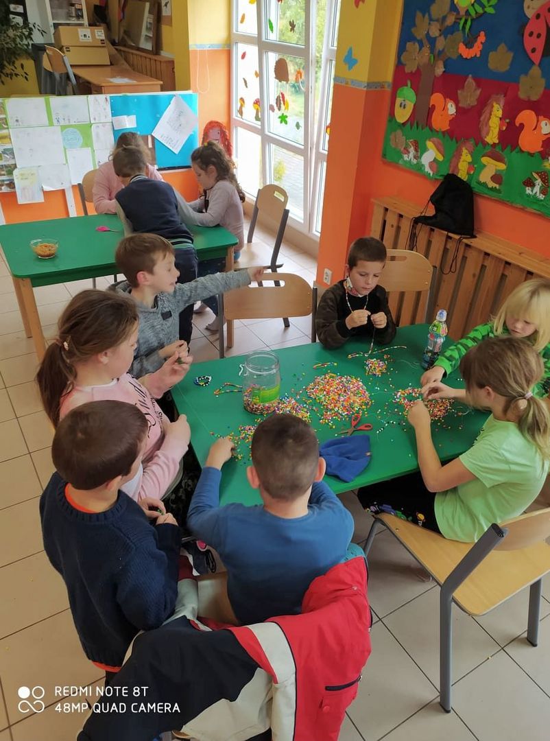 Dzieci z Placówki Wsparcia Dziennego z Lasek robią bransoletki z kolorowych koralików.