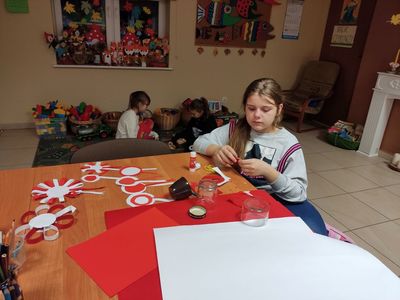 Dziewczynka z placówki wsparcia dziennego w Kosierzewie podczas  wykonywania  kotylionu, w tle dwie dziewczynki. 