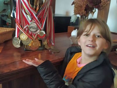 Dziewczynka z Placówki Wsparcia Dziennego z Lasek z medalami zdobytymi przez Olimpijczyka.

