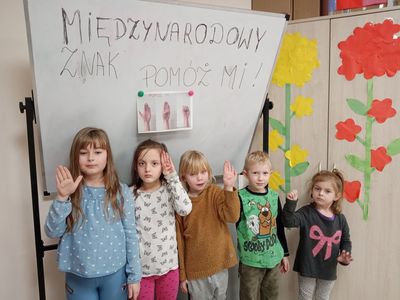 Dzieci z Placówki Wsparcia Dziennego w Niemicy  podczas zajęć profilaktycznych, pozują przy plakacie w geście "Pomóż mi".