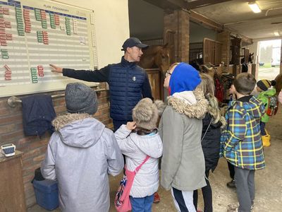 Paweł Spisak opowiada o tygodniowym planie pracy z końmi, dzieci słuchają uważnie. 