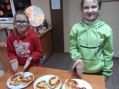 Dwie dziewczynki z Placówki Wsparcia Dziennego prezentują wykonane podczas zajęć kulinarnych pizzerki.