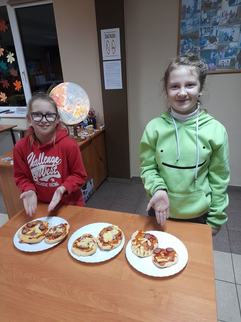 Dwie dziewczynki z Placówki Wsparcia Dziennego prezentują wykonane podczas zajęć kulinarnych pizzerki.