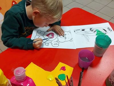 Wychowanek z PWD z Lasek maluje farbami kolorowankę misia.