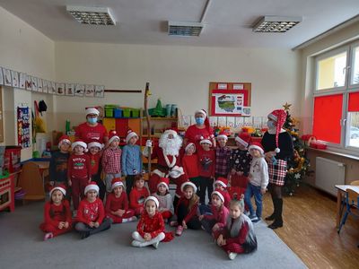 Dzieci  przedszkola w Ostrowcu ubrane w czapki mikołaja siedzą na dywanie.