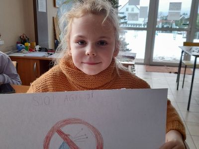 Dziewczynka z Placówki Wsparcia Dziennego w Sulechowie pozująca do zdjęcia z wykonanym przez siebie plakatem.