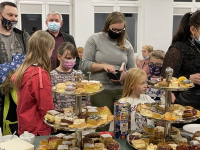 Zdjęcie uczestników 30. finału WOŚP w strefie słodkiej kawiarenki, na stole patery z ciastem oraz osoby oczekujące w kolejce.
