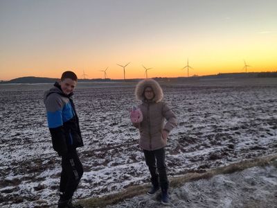 Dziewczynka i chłopiec z PWD w Sulechowie podczas spaceru. W tle pola i wiatraki.