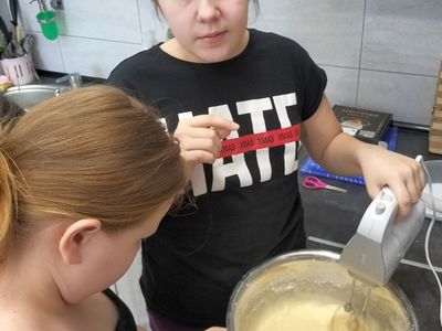 Dwie wychowanki z Placówki Wsparcia Dziennego w Kusicach przygotowują ciasto marchewkowe, miksują składniki mikserem i dodają je.